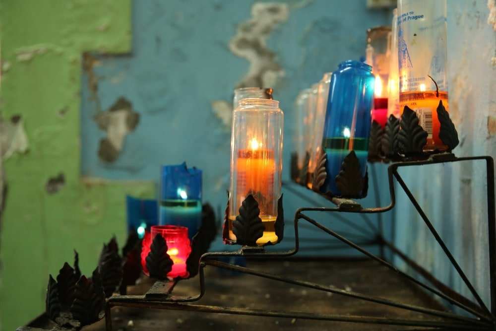 Photograph of multicolored religious candles in glass holders sitting in a multi-tiered metal rack.