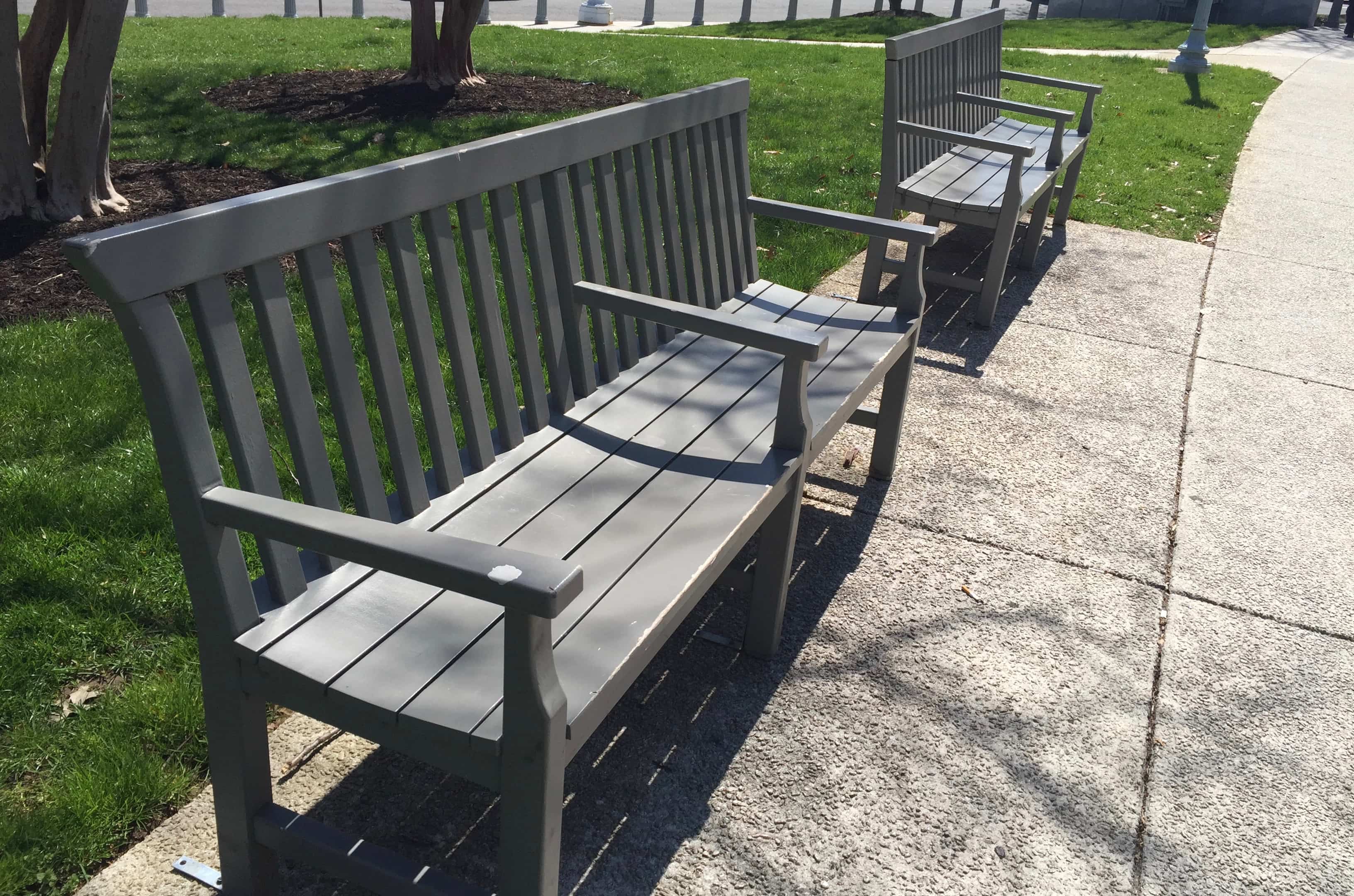 A photograph of two gray wood benches that each have a third armrest in the middle.