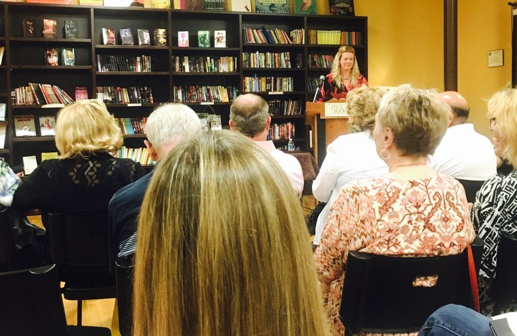 Alt Text: Photograph of the author Katie Rose Guest Pryal reading to a crowd at Flyleaf Books for the launch party for CHASING CHAOS. She stands behind a podium at the front of a room full of people.