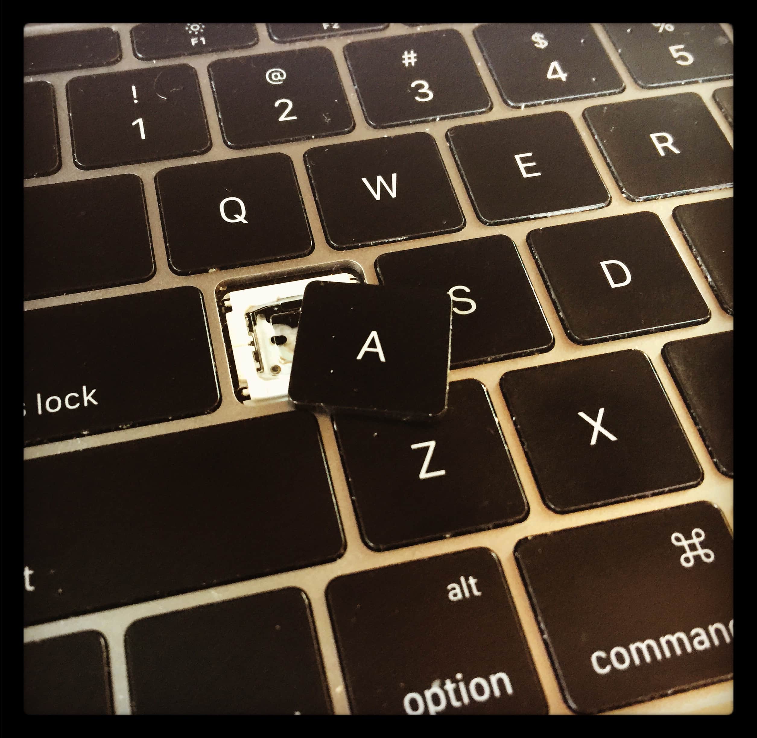 Alt Text: A photograph of my MacBook keyboard with the A key broken off and resting askew.