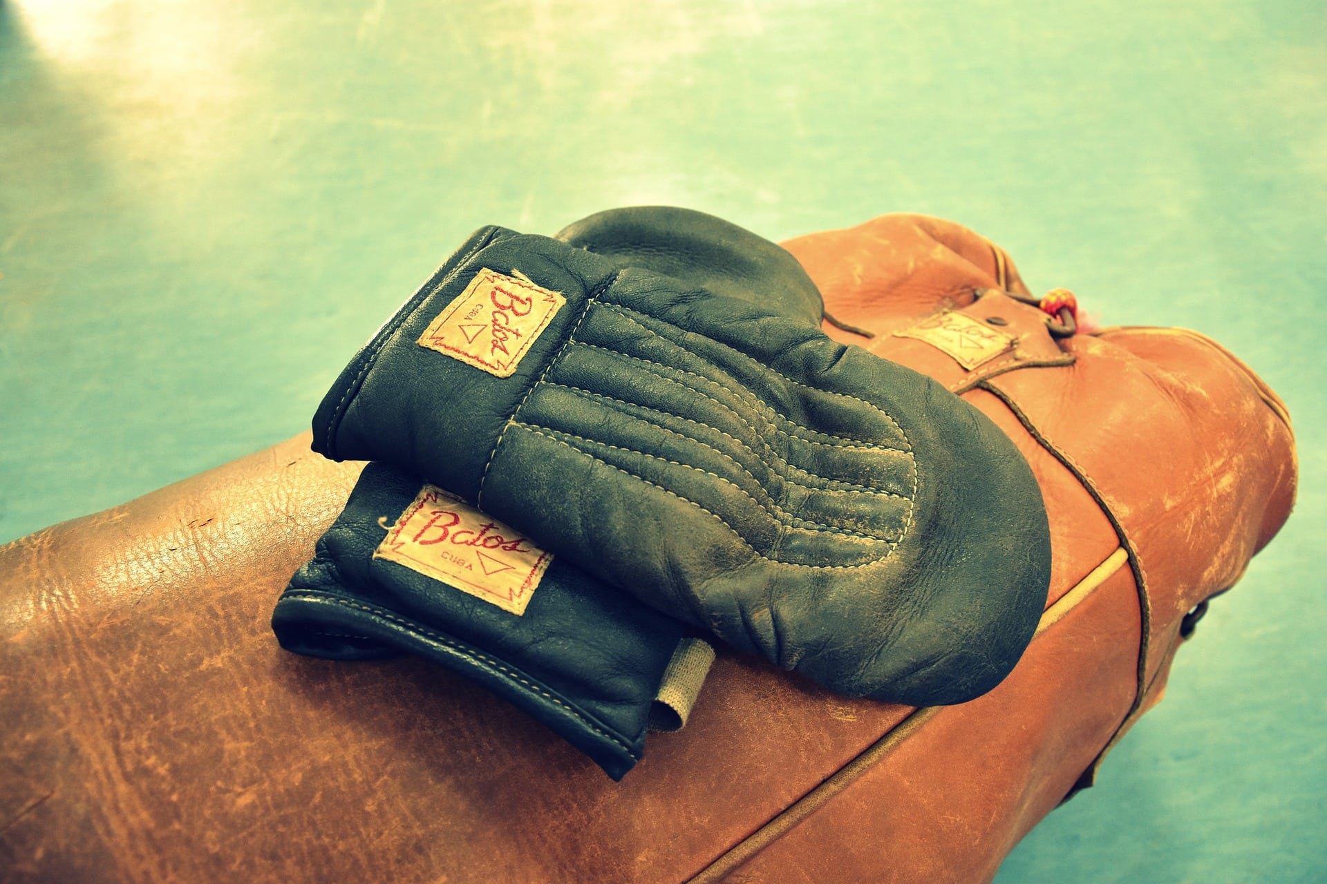 Image Alt-Text: A photograph of a pair of old-fashioned leather boxing gloves lying on a punching bag.